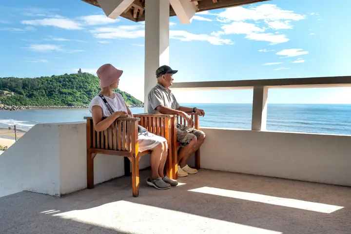 An older couple in sun hats sitting on a terrace over the sea