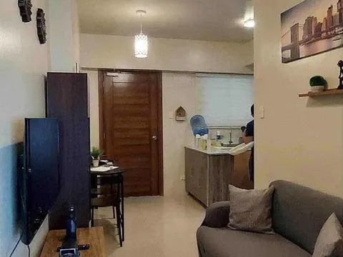 A simple furnished living room with a sofa, a TV and a ceiling fan