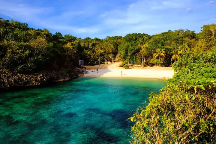 A small sandy cove with green cliffs and clear water